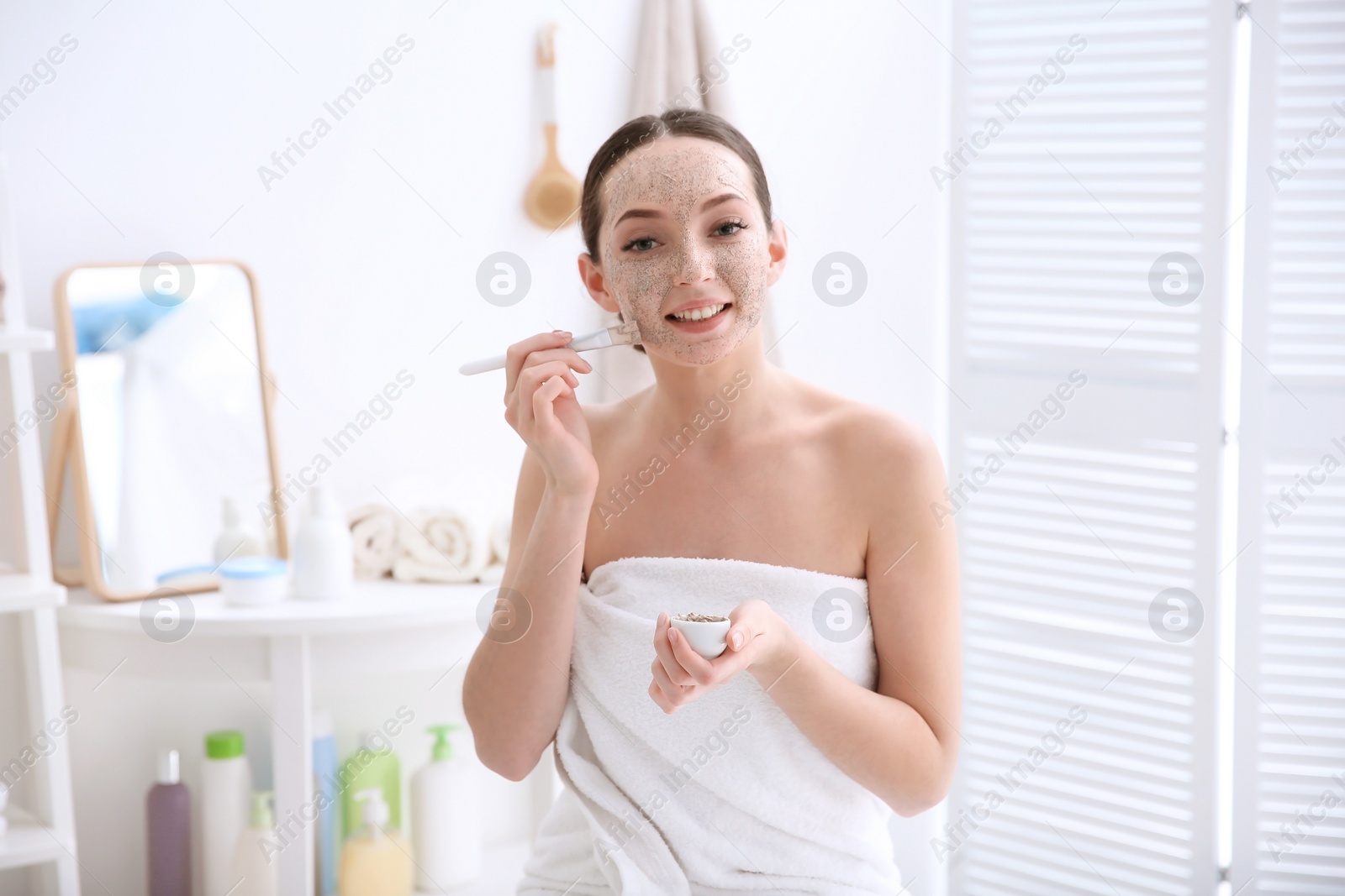 Photo of Woman applying scrub onto face in bathroom