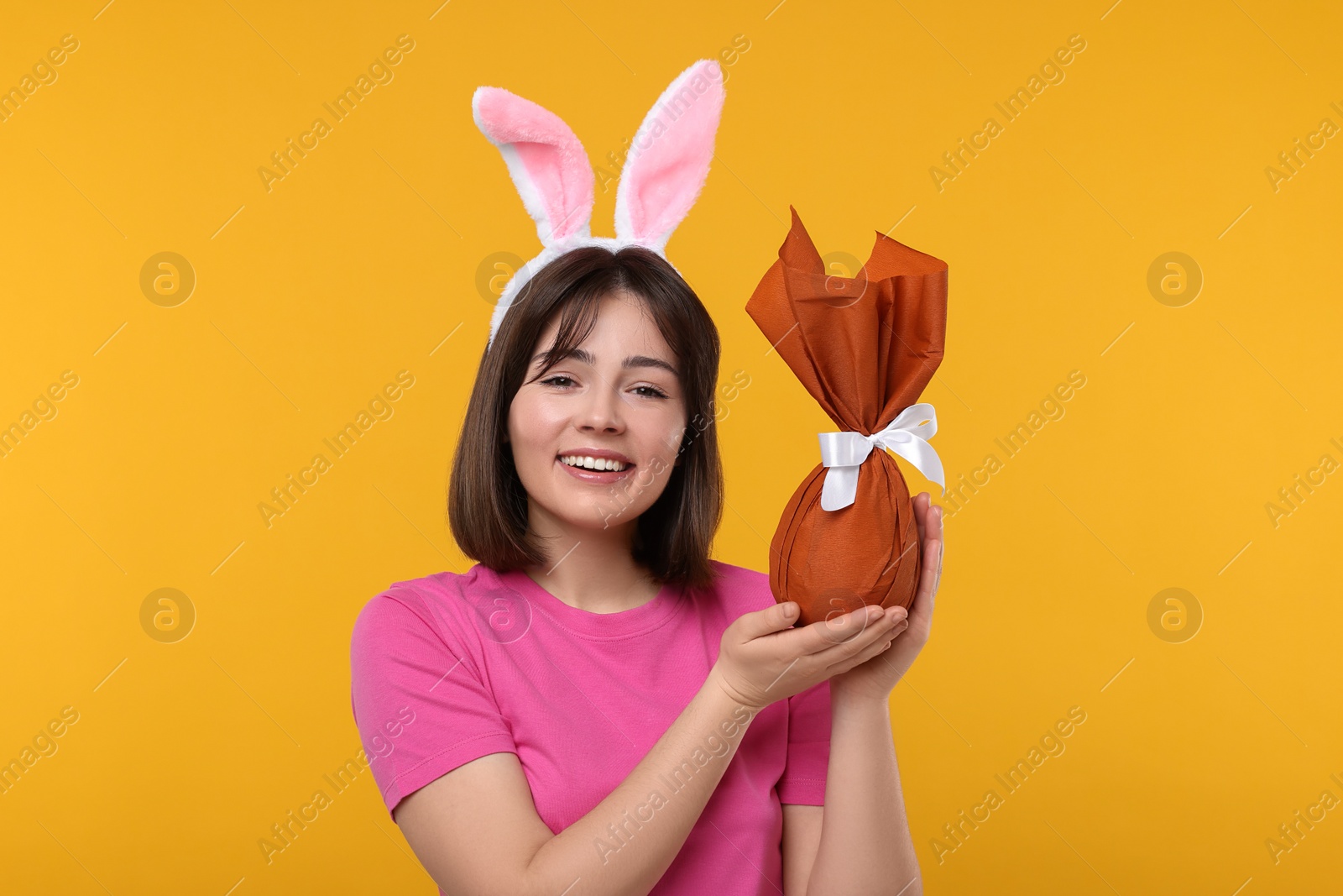 Photo of Easter celebration. Happy woman with bunny ears and wrapped egg on orange background