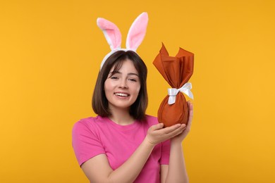 Easter celebration. Happy woman with bunny ears and wrapped egg on orange background