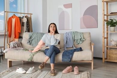 Photo of Thoughtful young woman on sofa with clothes at home