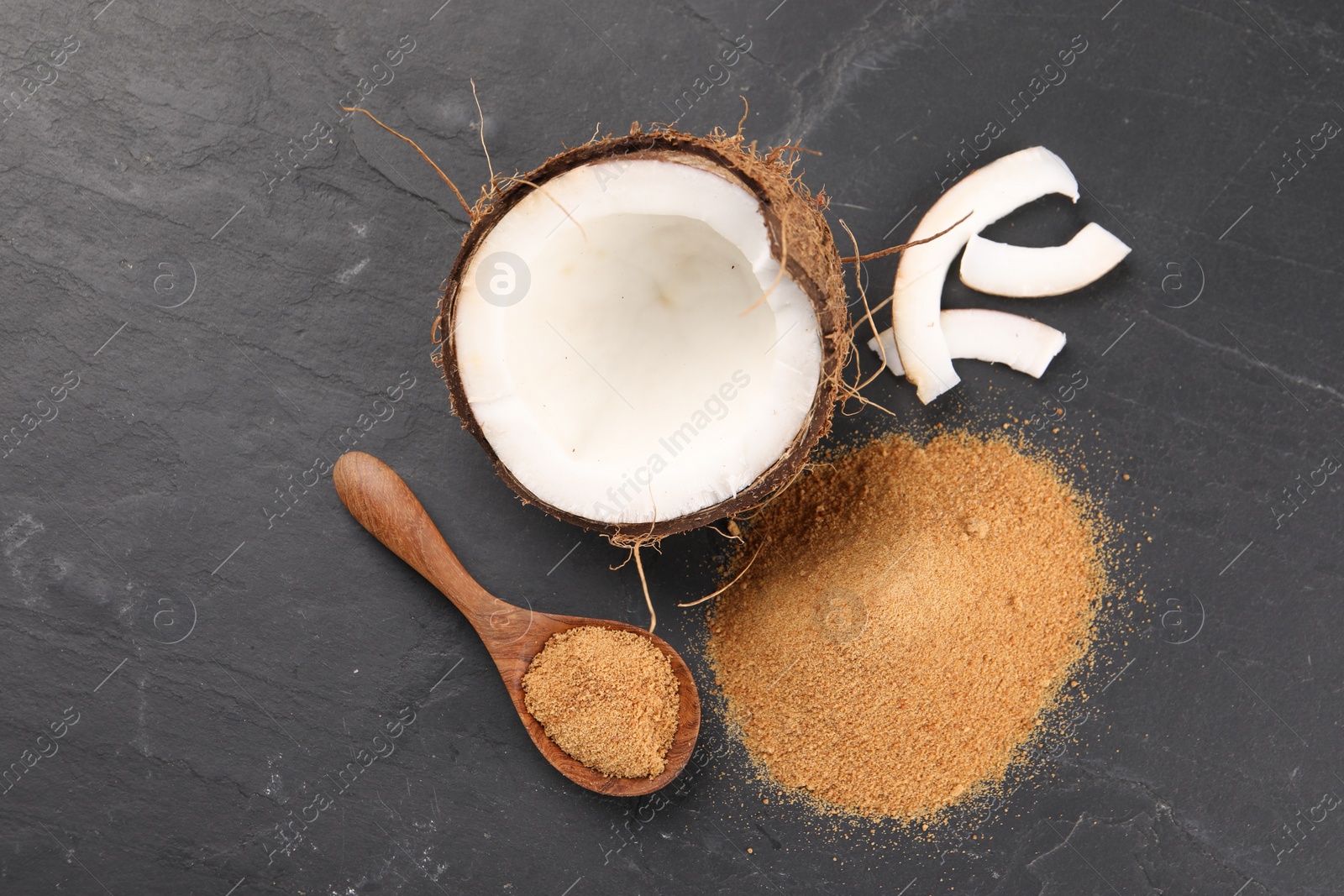 Photo of Coconut sugar, spoon and fruit on dark textured table, flat lay