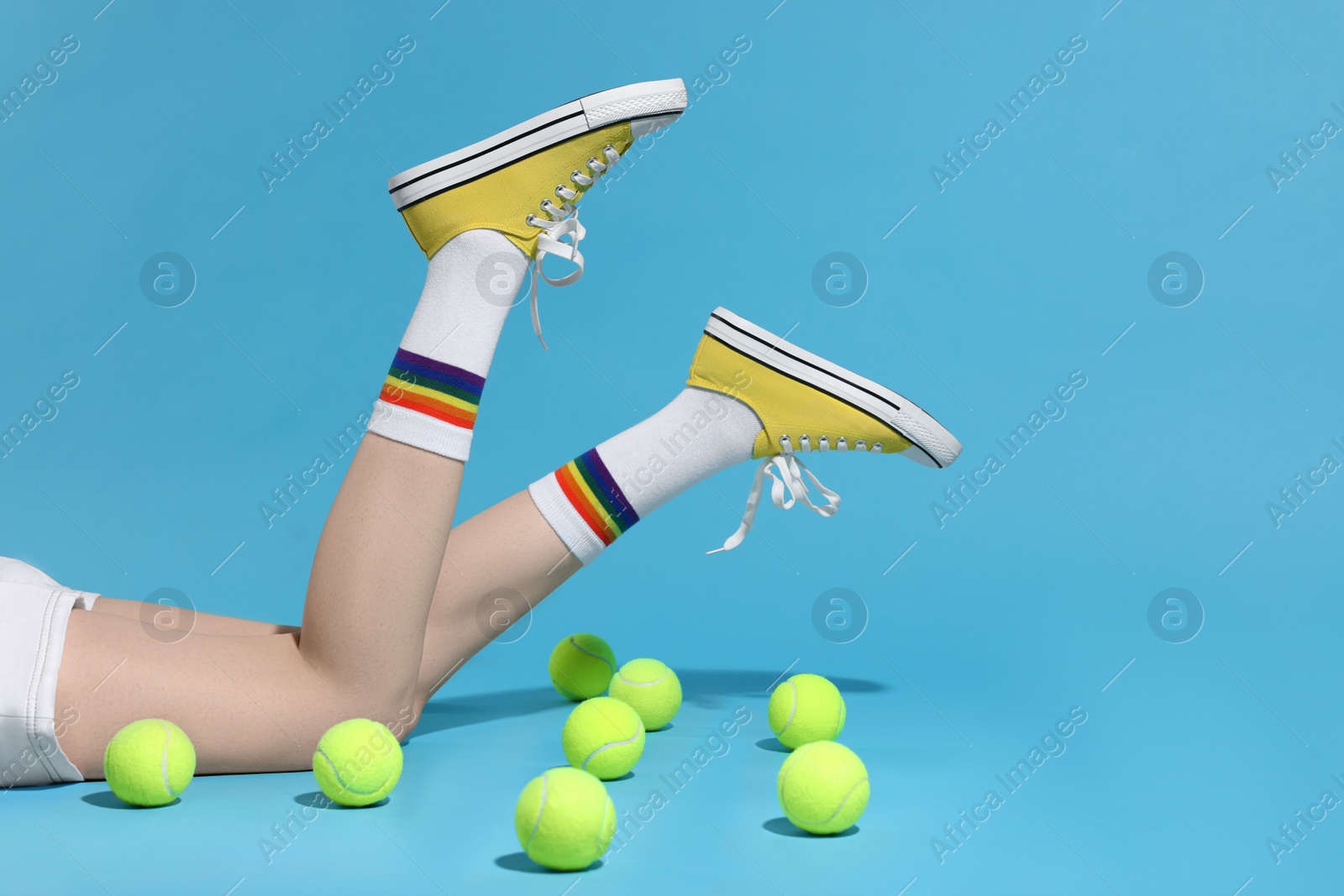 Photo of Woman posing in yellow classic old school sneakers and tennis balls on light blue background, closeup. Space for text