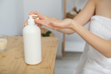 Photo of Young woman applying body cream on hands in bathroom, closeup