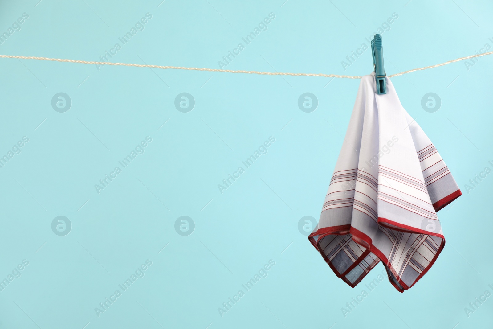 Photo of Handkerchief hanging on rope against light blue background, space for text