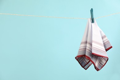 Handkerchief hanging on rope against light blue background, space for text