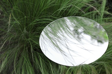 Round mirror on green grass. Space for text