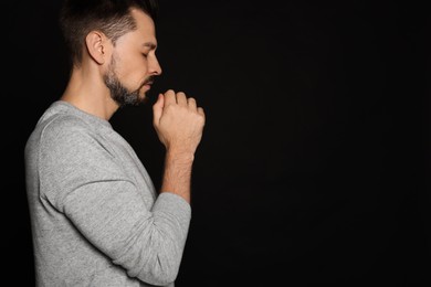 Photo of Man with clasped hands praying on black background. Space for text