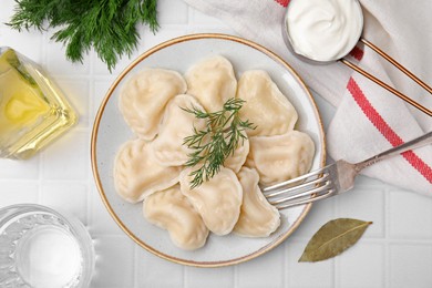 Photo of Cooked dumplings (varenyky) with tasty filling and sour cream on white tiled table, flat lay
