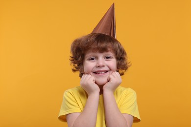 Photo of Happy little boy in party hat on orange background