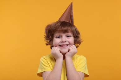 Happy little boy in party hat on orange background