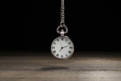 Photo of Beautiful vintage pocket watch with silver chain on black background above wooden table. Hypnosis session