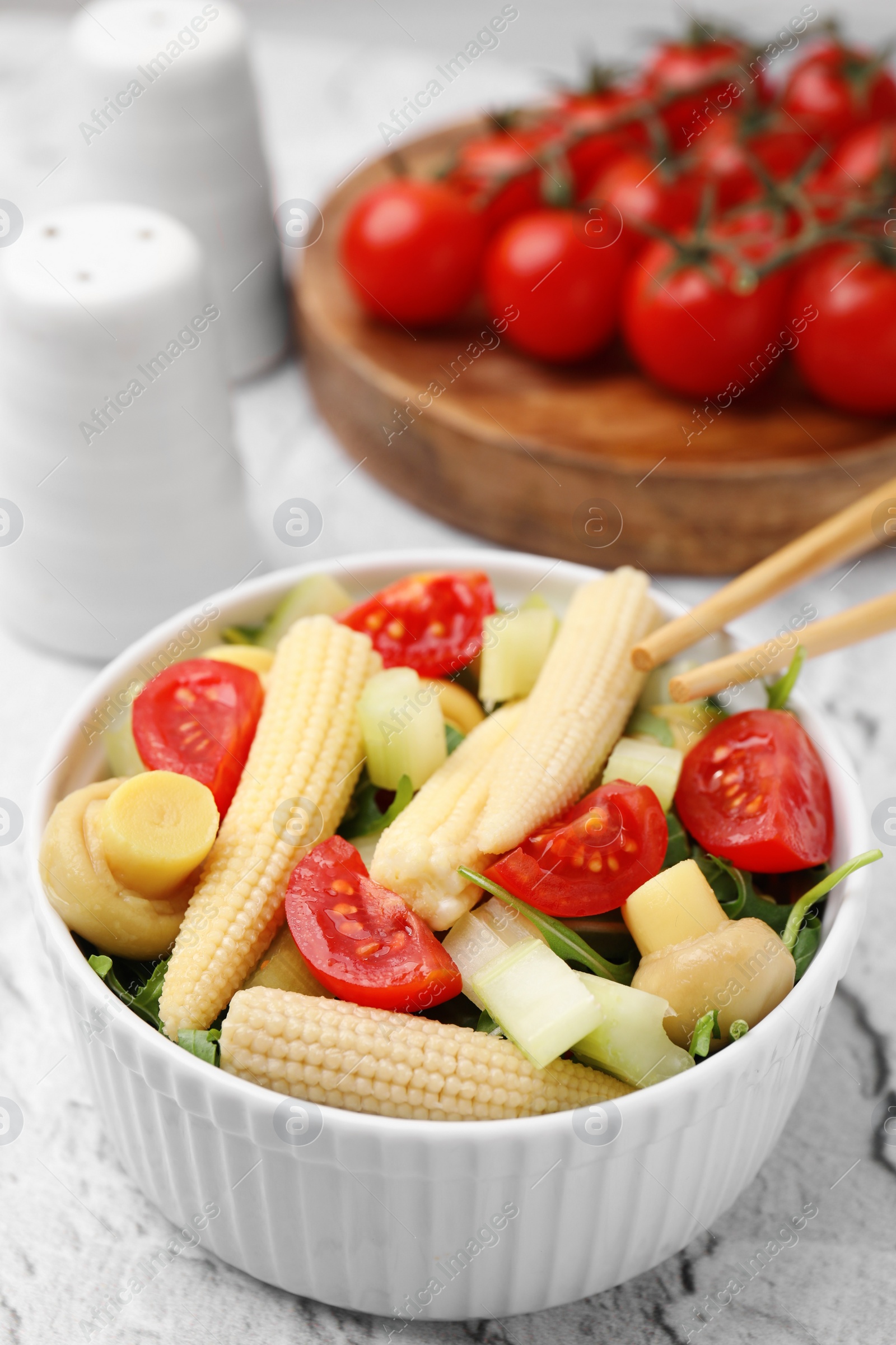 Photo of Tasty baby corn with vegetables and champignons on grey textured table, closeup