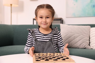 Photo of Cute girl playing checkers on sofa at home