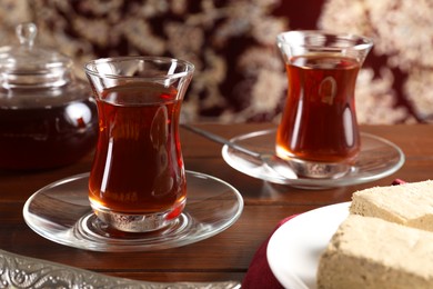Traditional Turkish tea in glasses and tasty halva on wooden table, closeup