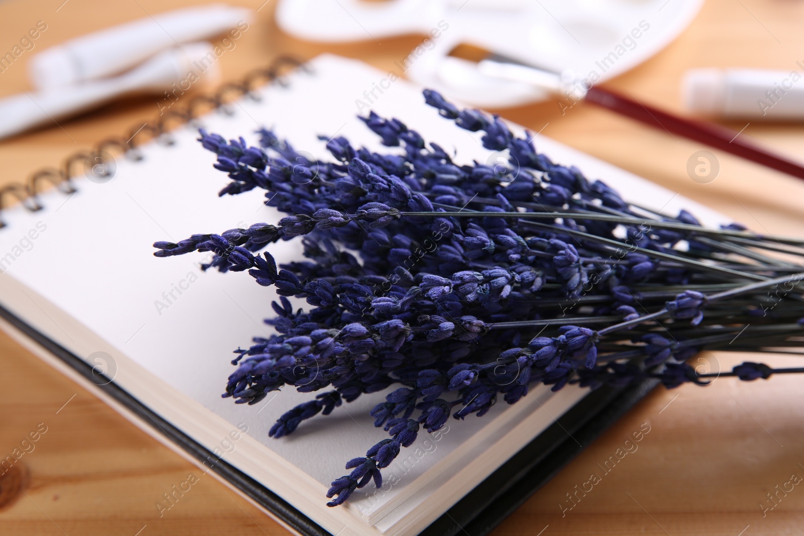 Photo of Bouquet of beautiful preserved lavender flowers and notebook on wooden table, closeup