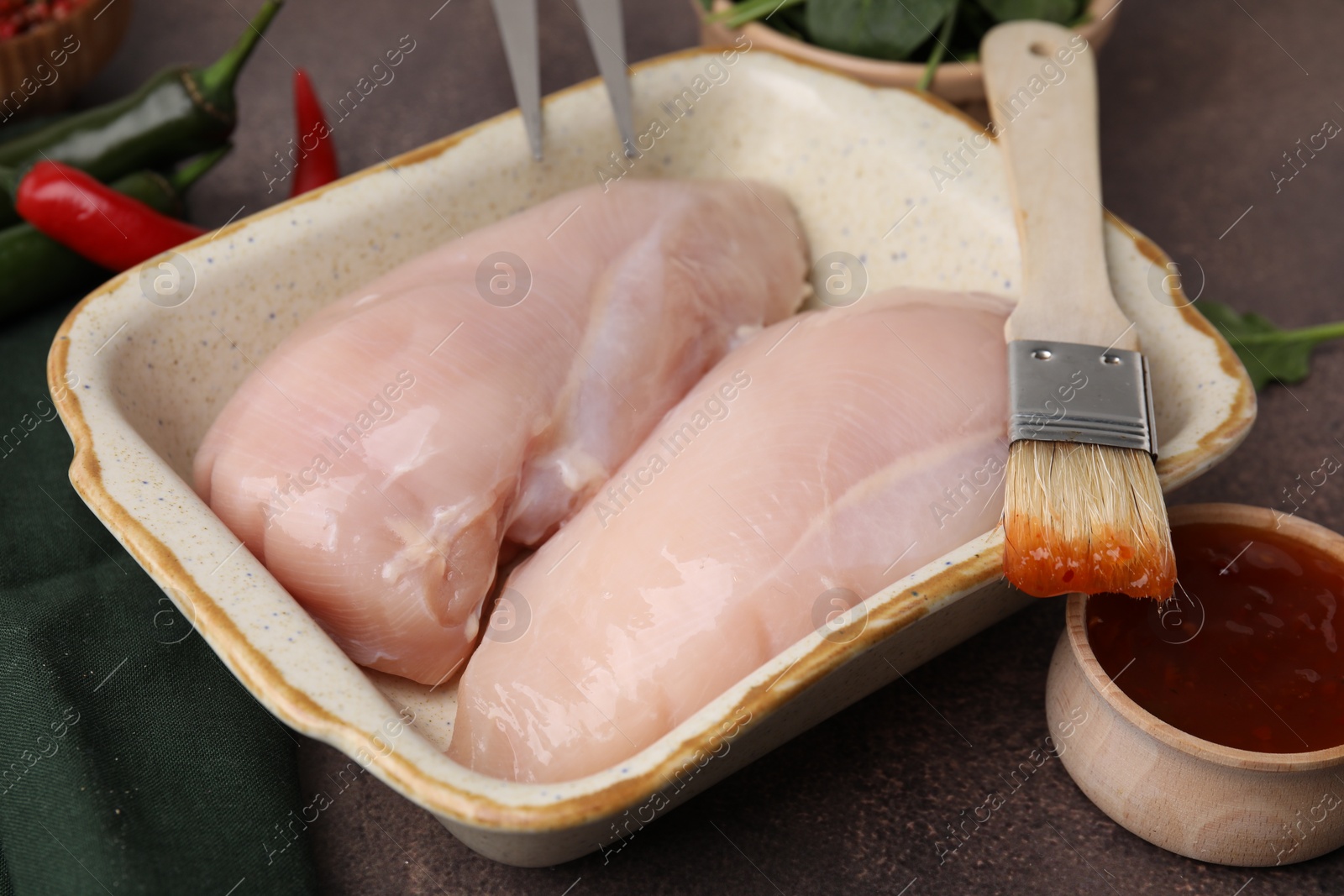 Photo of Marinade, basting brush and raw chicken fillets on brown table, closeup