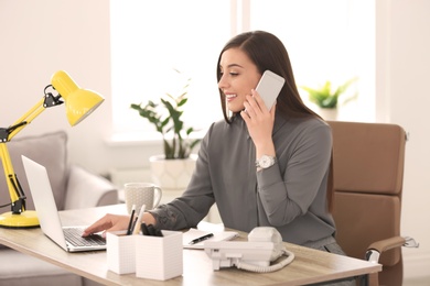 Photo of Young woman talking on phone at workplace