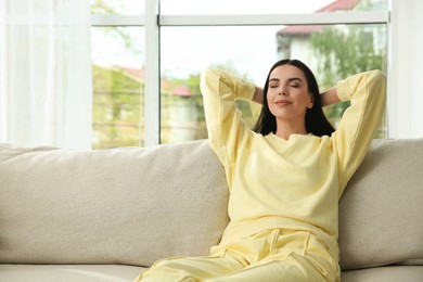 Young woman relaxing on sofa at home, space for text