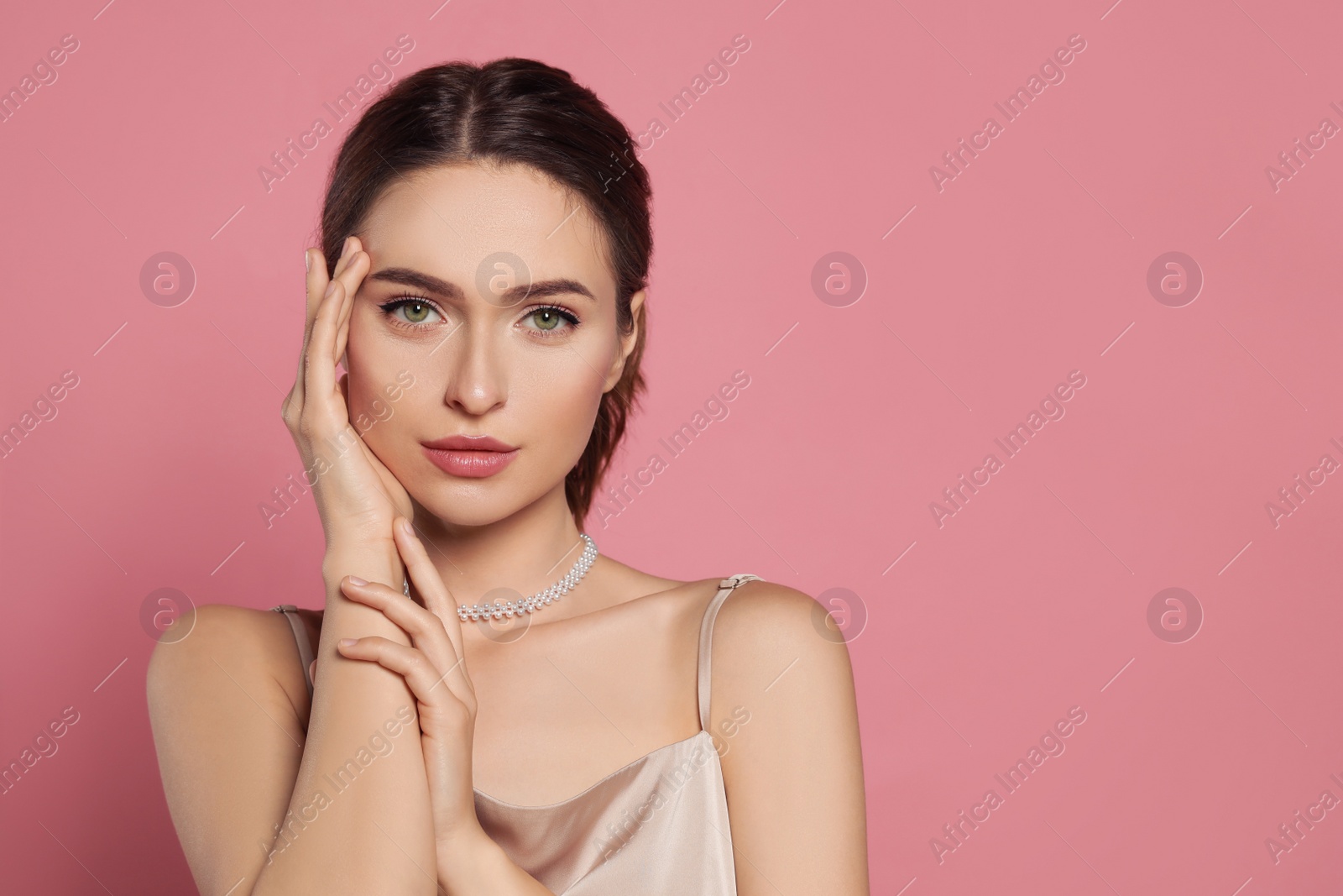 Photo of Young woman wearing elegant pearl necklace on pink background, space for text