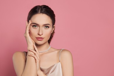 Young woman wearing elegant pearl necklace on pink background, space for text