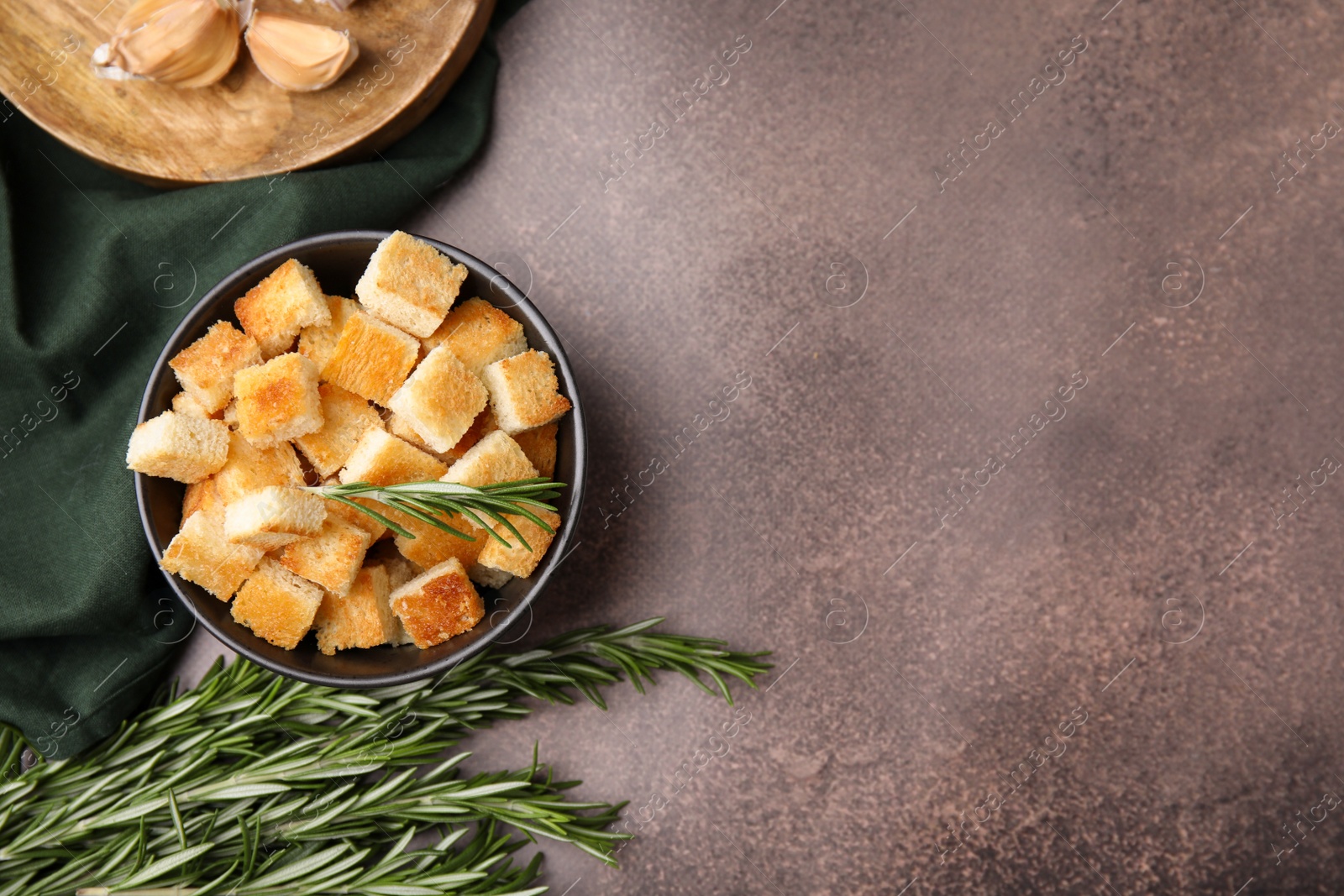 Photo of Delicious crispy croutons in bowl and rosemary on dark table, flat lay. Space for text