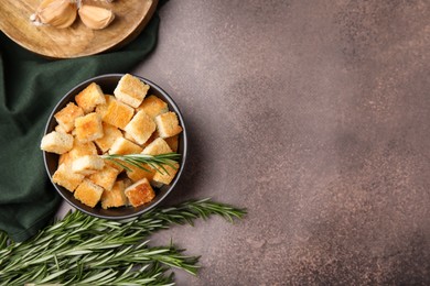 Photo of Delicious crispy croutons in bowl and rosemary on dark table, flat lay. Space for text