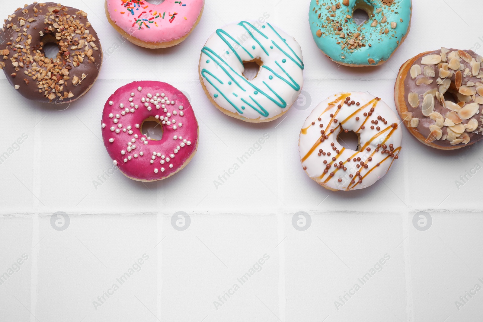 Photo of Different tasty donuts on white tiled table, flat lay. Space for text