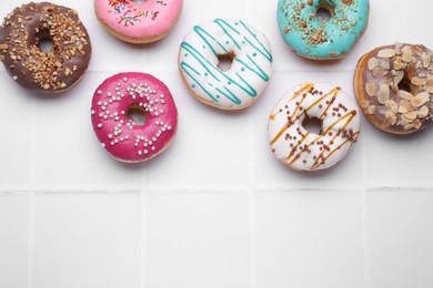 Different tasty donuts on white tiled table, flat lay. Space for text