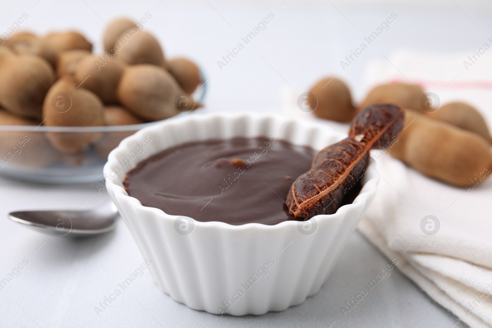 Bowl of tamarind sauce and fresh pods on light table, closeup Photo of Bowl of tamarind sauce and fresh pods on light table, closeup