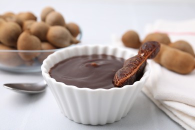 Photo of Bowl of tamarind sauce and fresh pods on light table, closeup