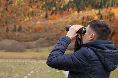 Photo of Boy looking through binoculars in beautiful mountains, back view. Space for text