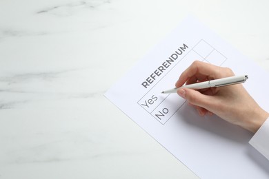 Woman with referendum ballot making decision at white marble table, closeup. Space for text