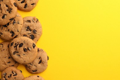 Photo of Many delicious chocolate chip cookies on yellow background, flat lay. Space for text