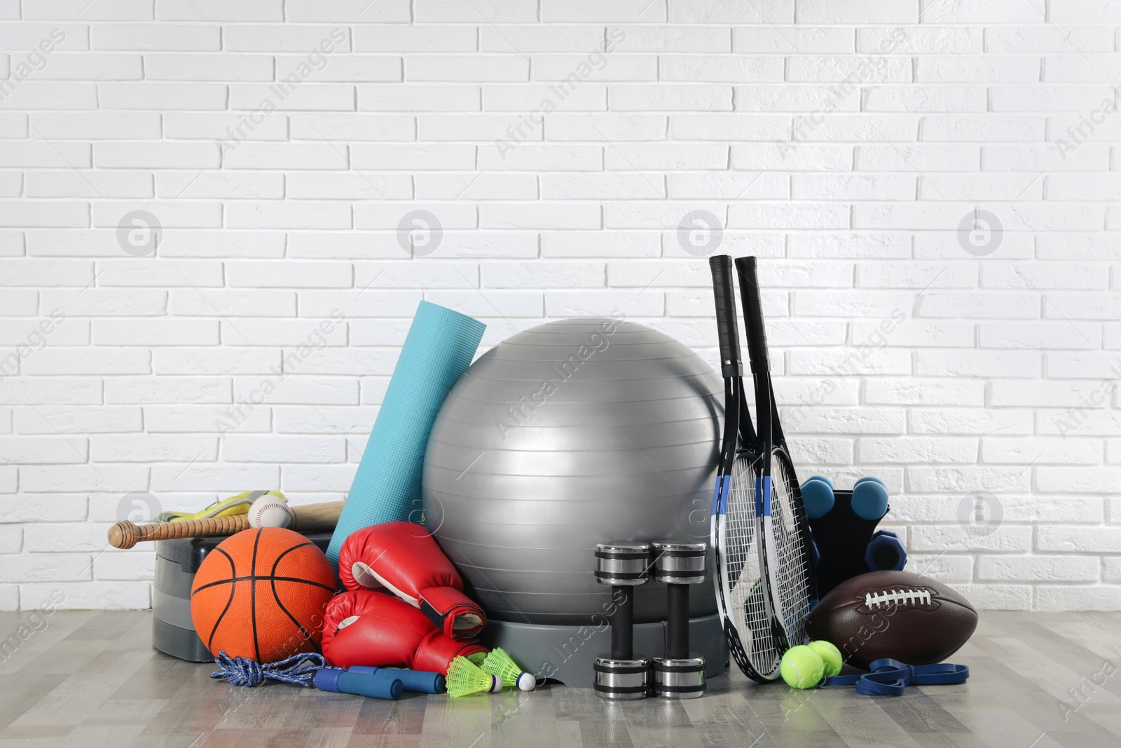 Photo of Set of different sports equipment on floor near white brick wall