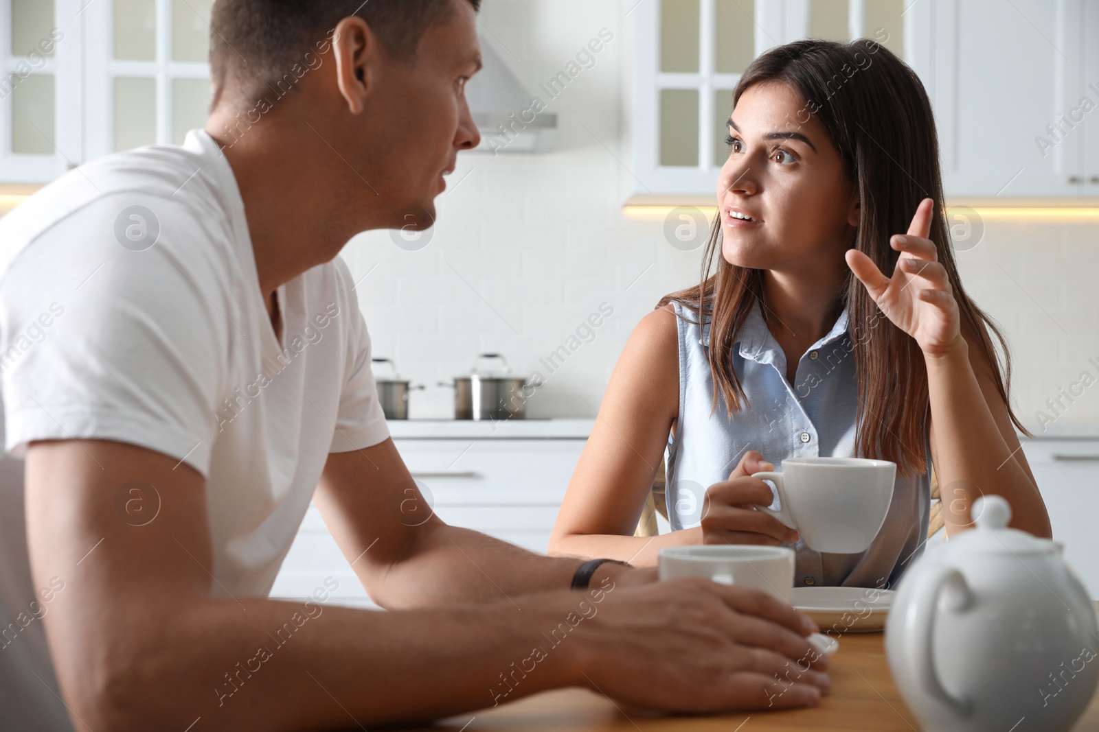 Photo of Man and woman talking while drinking tea at table in kitchen