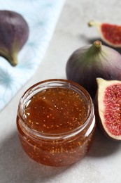 Jar of tasty sweet jam and fresh figs on light table, closeup