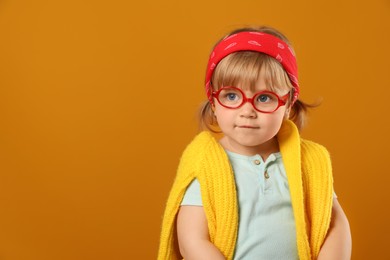 Photo of Cute little girl in glasses on orange background. Space for text