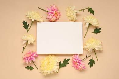 Photo of Beautiful chrysanthemums, leaves and blank card on beige background, flat lay. Space for text