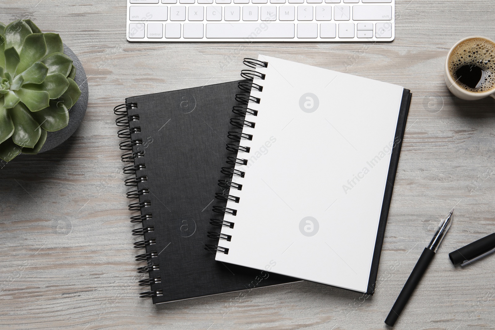 Photo of Notebooks, pen, coffee and keyboard on light wooden table, flat lay