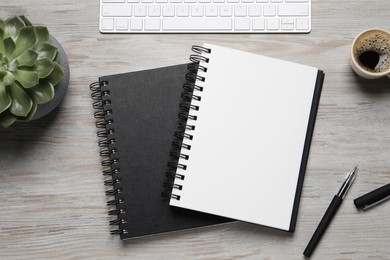 Notebooks, pen, coffee and keyboard on light wooden table, flat lay