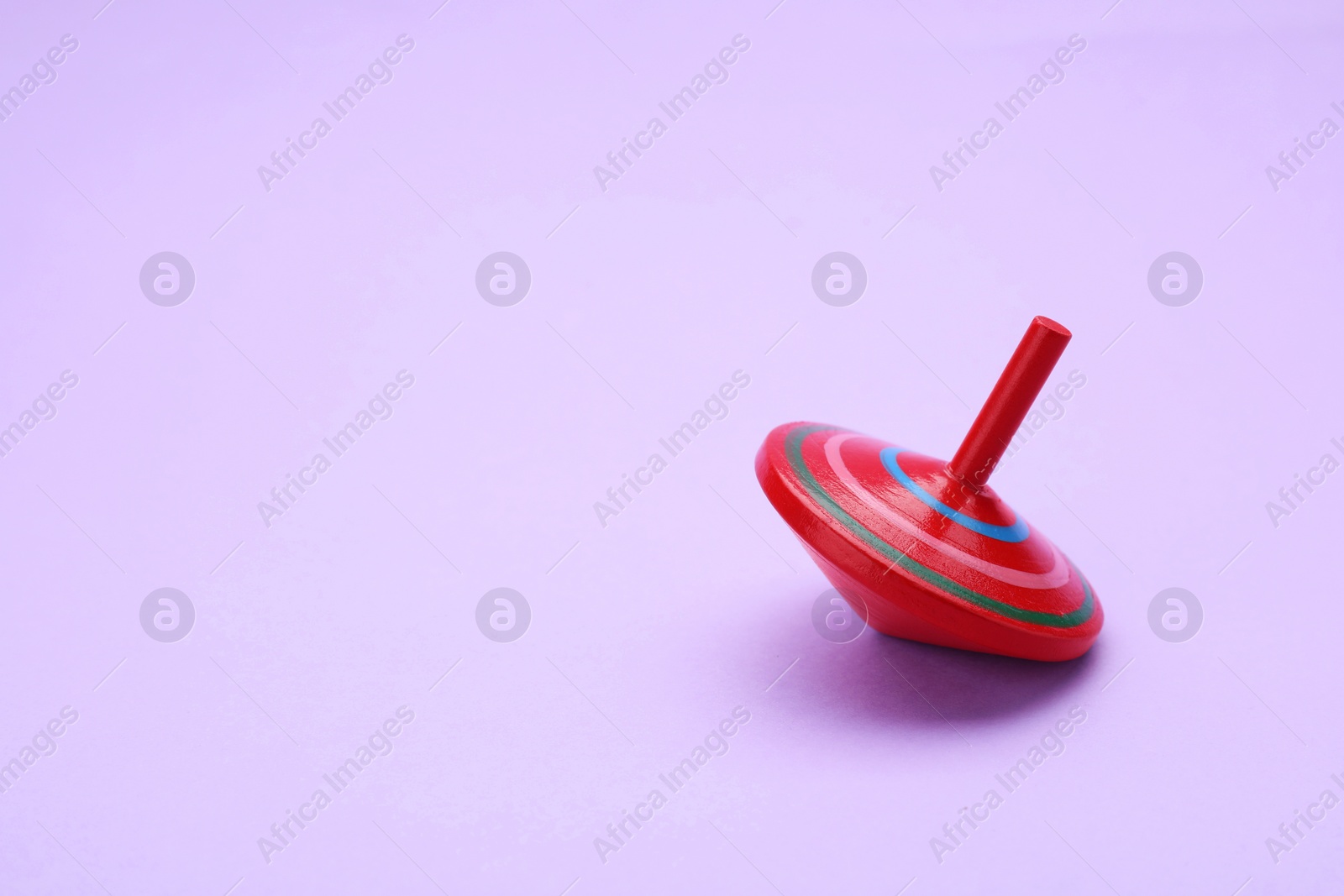 Photo of One bright spinning top on lilac background, space for text. Toy whirligig