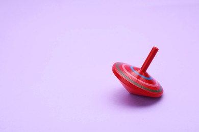 One bright spinning top on lilac background, space for text. Toy whirligig