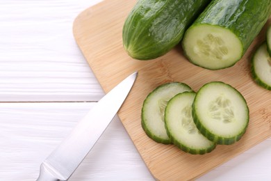 Photo of Cucumbers, knife and cutting board on white table, top view