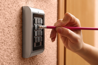 Photo of Woman using pencil to enter code on electronic lock's keypad indoors, closeup