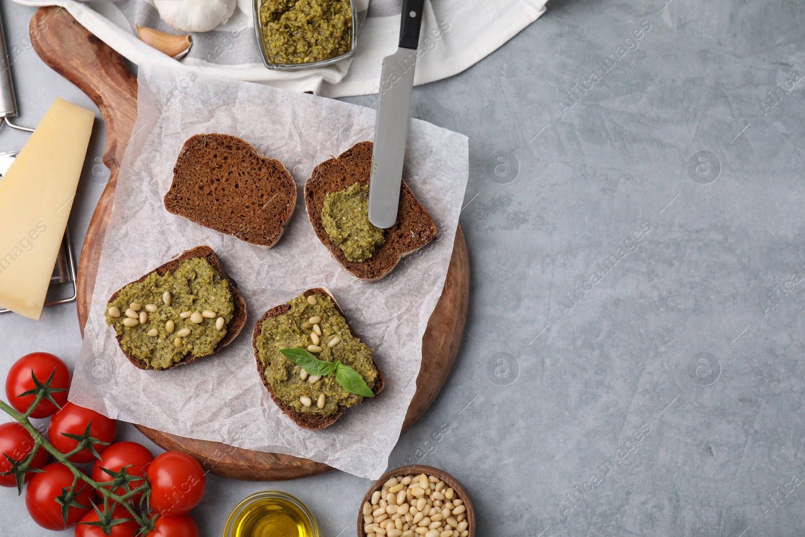 Photo of Making delicious bruschettas with pesto sauce, nuts and fresh basil on light grey table, flat lay. Space for text