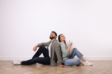 Photo of Young couple sitting on floor near white wall indoors