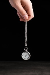 Photo of Psychotherapist with pendulum on black background, closeup. Hypnotherapy session