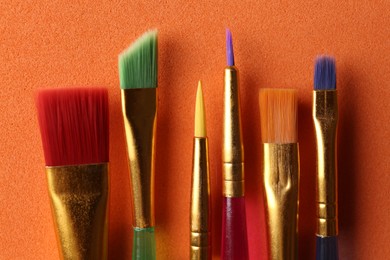 Photo of Set of different paintbrushes on orange background, flat lay