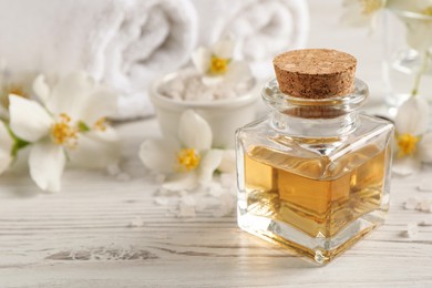 Beautiful composition with jasmine essential oil and fresh flowers on white wooden table. Space for text