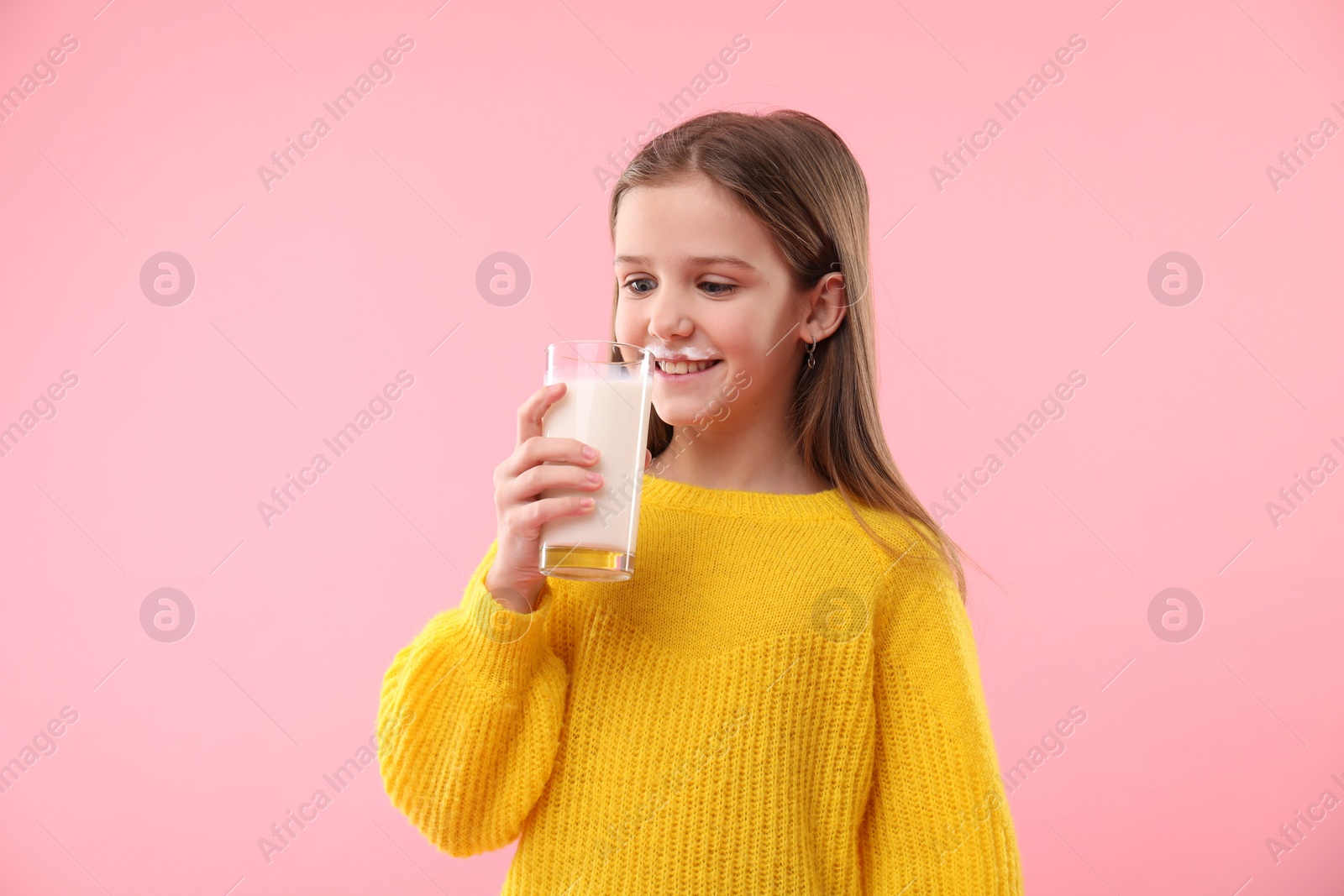 Photo of Happy little girl with milk mustache holding glass of tasty dairy drink on pink background